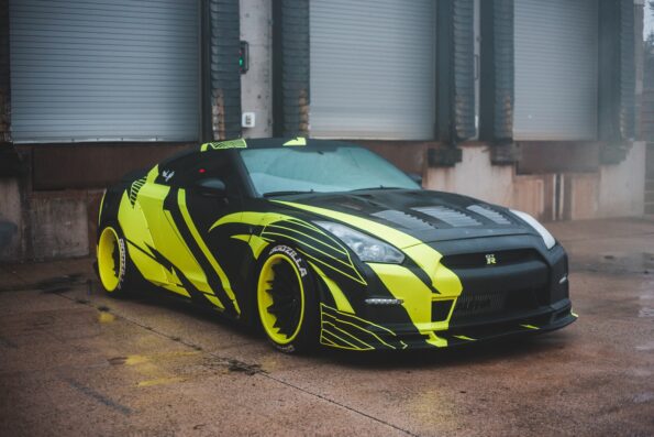 Luxury sports car with yellow wrapping decal design parked on pavement near industrial building with closed blinds in city on street